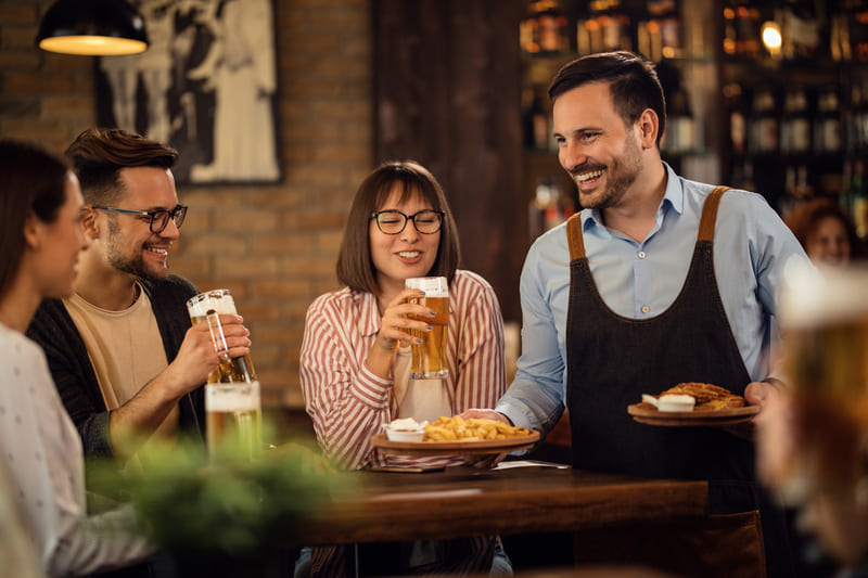 Como abrir CNPJ para restaurante - Imagem pequeno grupo de amigos felizes bebendo cerveja enquanto o garcom esta servindo um lanche em uma taverna
